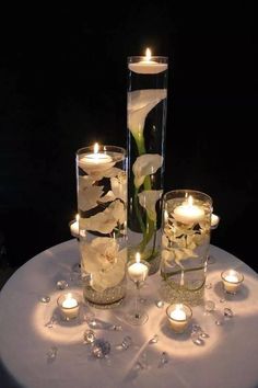 white flowers and candles in glass vases on a round table with silver clothing