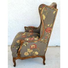 an old fashioned chair with floral fabric on the back and arms, in front of a white wall