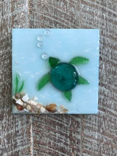 a glass tile with sea shells and a green turtle on it's back side