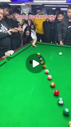 a group of people standing around a green pool table with balls on it and one person reaching for the ball