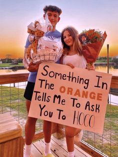 a man and woman standing on a porch holding flowers, one is holding a sign that says something in the orange tells me to ask you to hoo