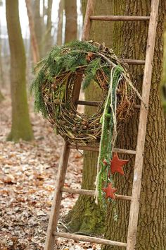 an old ladder is decorated with wreaths and leaves in the woods near a tree