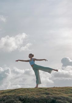 a woman standing on top of a grass covered hill with her arms outstretched in the air