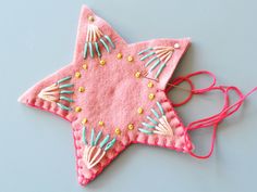 a pink felt star ornament hanging from a string on a gray surface with beads