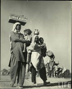 an old black and white photo shows people carrying items on their heads in the desert