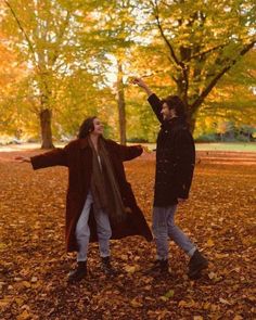 two people standing in the leaves with their arms outstretched