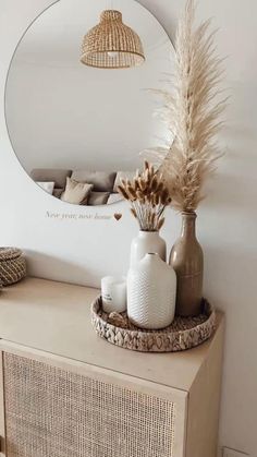 a vase with dried flowers on top of a dresser next to a round mirror and wicker basket