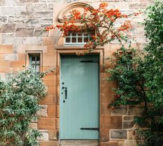 a blue door is in front of a brick building with red flowers on the tree