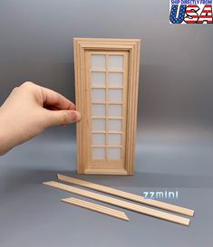 a hand is holding a wooden window and two pieces of wood are next to it