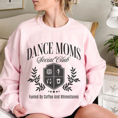 a woman sitting on top of a bed wearing a pink sweatshirt that says dance moms