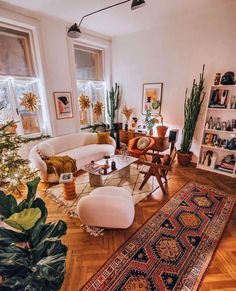 a living room filled with lots of furniture and plants on top of a hard wood floor