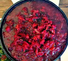 a pot filled with red food sitting on top of a wooden table next to vegetables