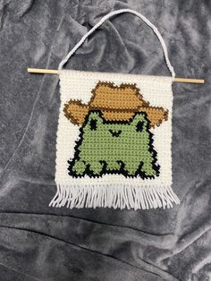 a crocheted wall hanging with a green frog wearing a cowboy hat on it