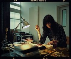 a woman sitting at a desk in front of a lamp and books on the table