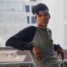 a young man leaning against a fence with his hands on his hips