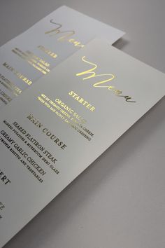 a close up of a menu on top of a white table with yellow lettering and gold foil