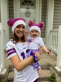 a woman holding a baby in her arms and wearing football outfits on the front steps of a house