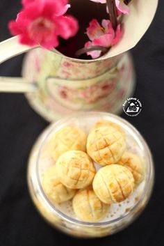 a pitcher filled with pink flowers next to some small pastries in a glass bowl