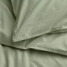 an unmade bed with green sheets and pillows