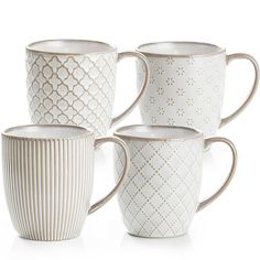 four white coffee mugs sitting next to each other on a white surface with an intricate design