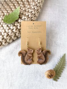 Title: Red Squirrels Looking for a unique handmade addition to your jewelry box? This pair of lovingly hand-painted wooden earrings will add artistic flair to your wardrobe or a personal touch to your gift to a loved one.  These original handcrafted earrings are hand painted on balsa wood with sterling silver hooks for sensitive ears (the gold hooks are gold plated sterling silver). Each pair of earrings in my shop is carved and painted by hand, and the item you receive is the exact one seen in the photos. The earrings are lightweight and hypoallergenic. This gift can be personalized with a special note and sent directly to friend or loved one. Please add the note during checkout using the box Etsy provides for "Notes to Seller." Looking for a different design? Check out my shop to find ot Artistic Hand Painted Brown Earrings, Skunk Jewelry, Racoon Earrings, Brown Bear Earrings, Squirrel Earrings, Red Squirrel, Animal Earrings, Handcrafted Earrings, Wooden Earrings