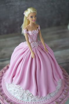 a barbie doll cake with pink dress and white lace on it's edge, sitting on a plate