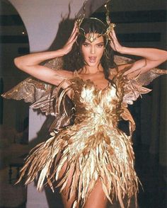 a woman in a gold dress with wings on her head and hands behind her head