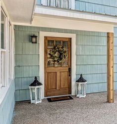 two white lanterns sitting on the front porch of a blue house with a wooden door