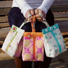 a woman sitting on a bench holding four purses in her hands, both with zippered handles