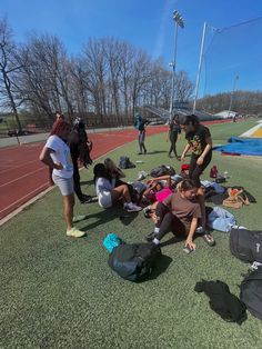 several people sitting on the ground with sports equipment around them and one person standing in the background