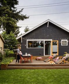 a woman standing on top of a wooden deck in front of a blue house with lawn chairs