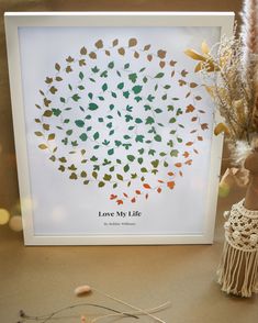 a white frame with leaves on it next to a vase and some dried flowers in the background