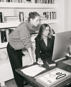 two women looking at a computer screen in front of a bookshelf full of books