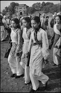 an old black and white photo of people walking in the dirt with one woman wearing a tie