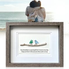 two people sitting on top of a wooden frame next to the ocean with a message written in it