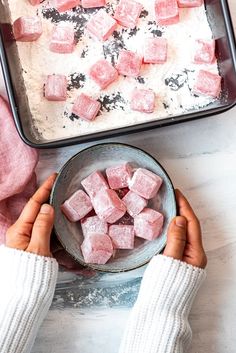 two hands holding a bowl with sugar cubes in it next to a baking pan