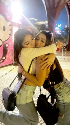 two young women hugging each other in front of a hello kitty sign at night time