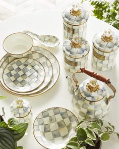 a white table topped with dishes and plates covered in glass mosaic tiles next to potted plants