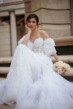 a woman in a white wedding dress sitting on steps with her hand to her face