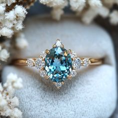 a blue and white diamond ring sitting on top of a cushioned surface next to some flowers