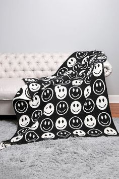 a black and white blanket sitting on top of a floor next to a couch covered in smiley faces