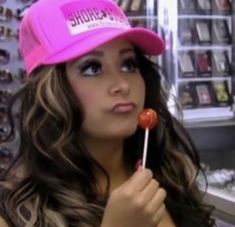 a woman holding a lollipop in her right hand and wearing a pink hat