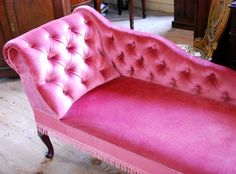 a pink couch sitting on top of a hard wood floor next to a wooden dresser