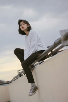 a woman sitting on top of a white wall next to a metal railing and looking up at the sky