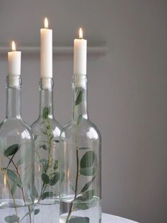 three glass bottles with plants in them sitting on a table next to two lit candles