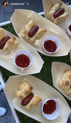 hotdogs with ketchup in paper bowls on trays sitting on grass