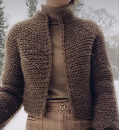 a woman standing in the snow wearing a brown sweater and plaid pants with her hands on her hips