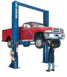 a man working on a red truck in a lift area with another person standing next to it