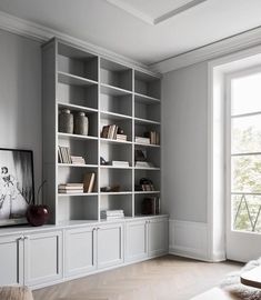 an empty living room with bookshelves and a television on the wall, in front of a large window