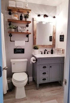 a white toilet sitting next to a bathroom sink under a wooden mirror mounted above it